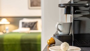 A coffee machine with a cup of coffee, a plate with a pastry, and a bed with a green bedspread in the background. - Sweett | Monsigny V - One Bedroom Apartment, Sleeps 3 (Paris)