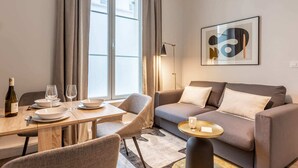 A modern living room with a dining area, a sofa, a coffee table, and a floor lamp. - Sweett | Monsigny V - One Bedroom Apartment, Sleeps 3 (Paris)