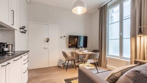 A modern living room with a sofa, a dining table with chairs, a TV, and a kitchen area with cabinets and a countertop. - Sweett | Monsigny V - One Bedroom Apartment, Sleeps 3 (Paris)