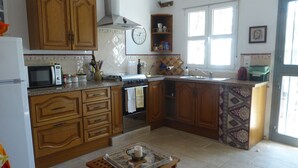 Una cocina con armarios de madera, microondas, estufa y fregadero. Hay una ventana que proporciona luz natural y un reloj en la pared.