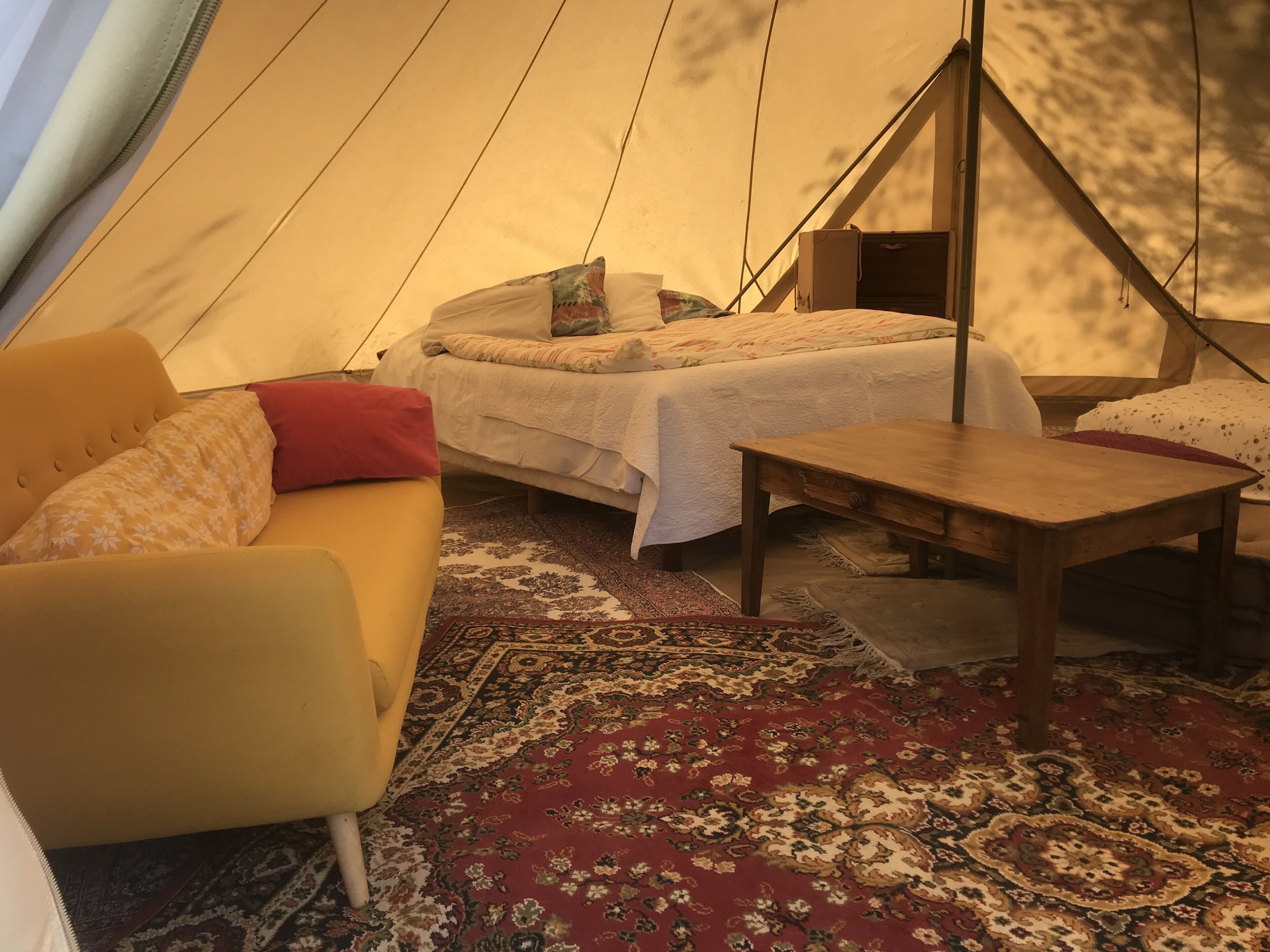 A cozy tent interior with a bed, a sofa, and a small table.