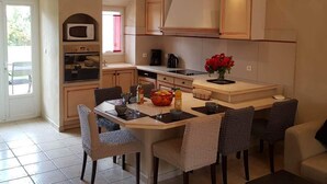 Een moderne keuken met een centraal eiland, inbouwapparatuur en een eethoek met stoelen.