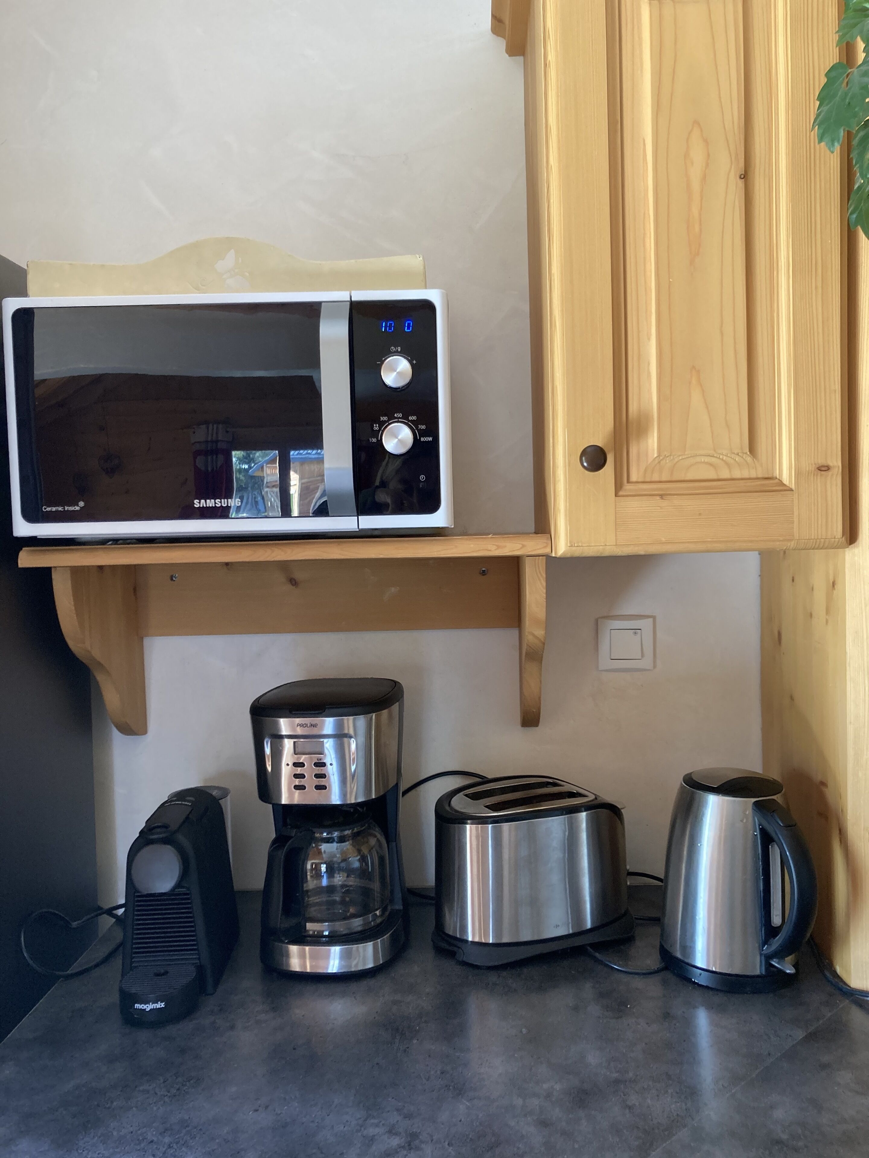 Een keuken met een magnetron op een houten plank, een koffiezetapparaat, een broodrooster en een waterkoker op het aanrecht.