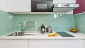 A modern kitchen with a stainless steel sink, a kettle, and a fruit bowl.