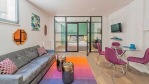A modern living room with a grey sofa, a coffee table, and a glass partition leading to a bedroom.