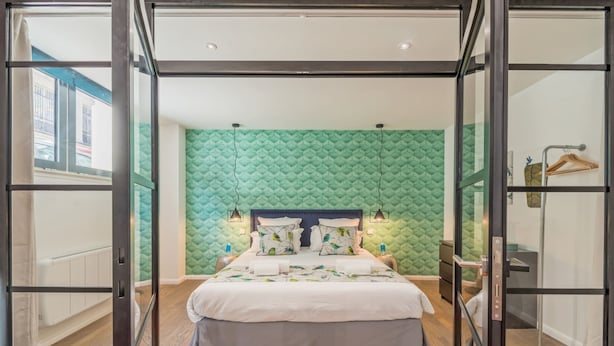 A modern bedroom with a green textured wall, a large bed with a white and gray bedspread, and a wooden floor.