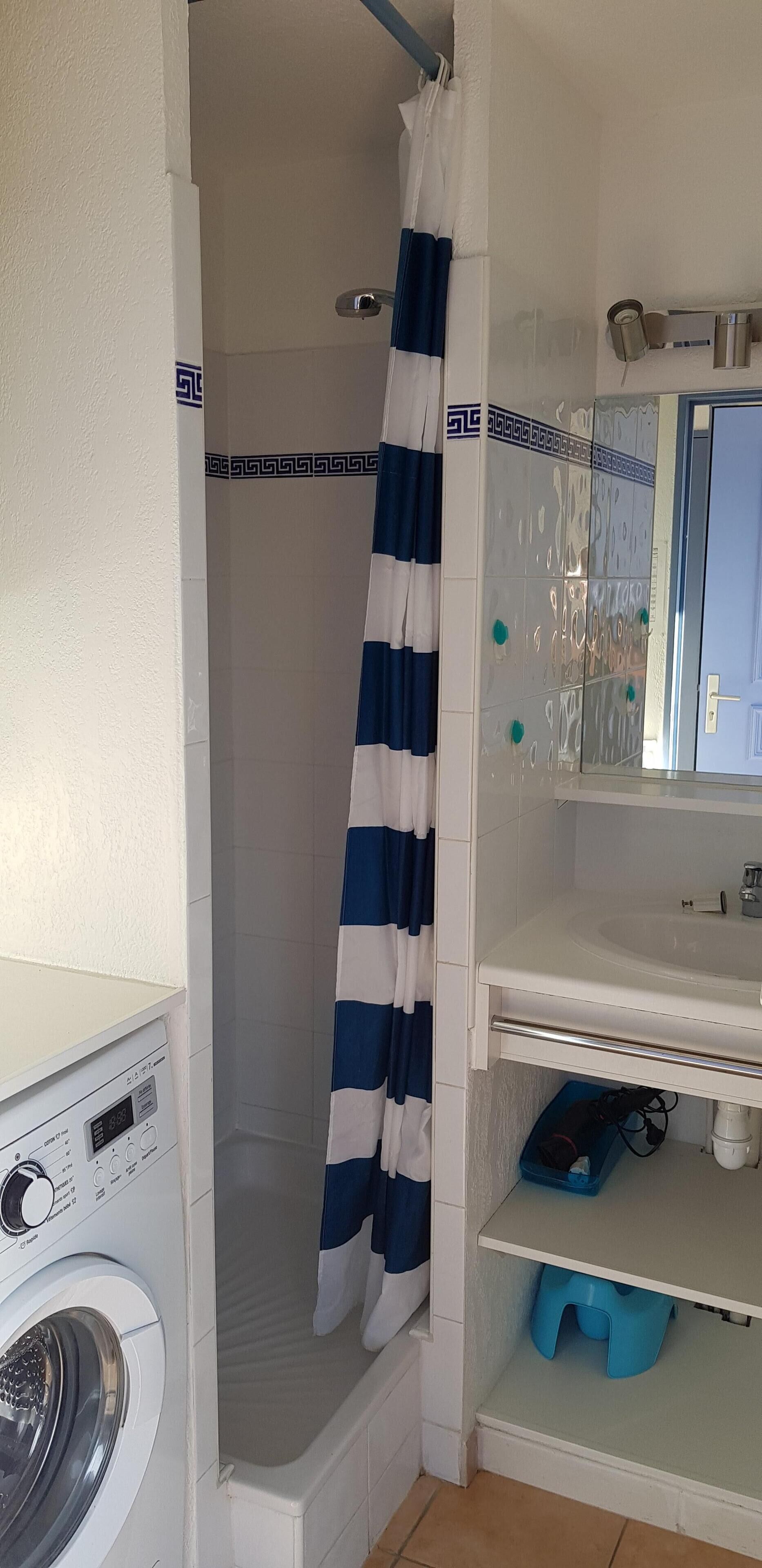 Une petite salle de bain comprenant une douche, un lave-linge et un lavabo avec un miroir.