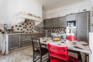 Une cuisine avec un sol carrelé à motifs, une table à manger avec des chaises rouges et un îlot central blanc doté d’un évier.