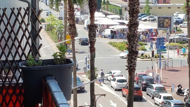 A balcony with a view of a busy street lined with palm trees and parked cars. - Apartment F3 of 90 M2 near the sea (Cagnes-Sur-Mer)