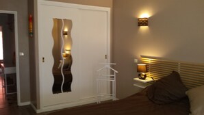 A hotel room with a white wardrobe, a bedside table with a lamp, and a bed with a headboard. - Apartment F3 of 90 M2 near the sea (Cagnes-Sur-Mer)
