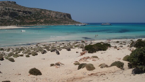 A beach with clear turquoise waters, boats, and rocky terrain.
