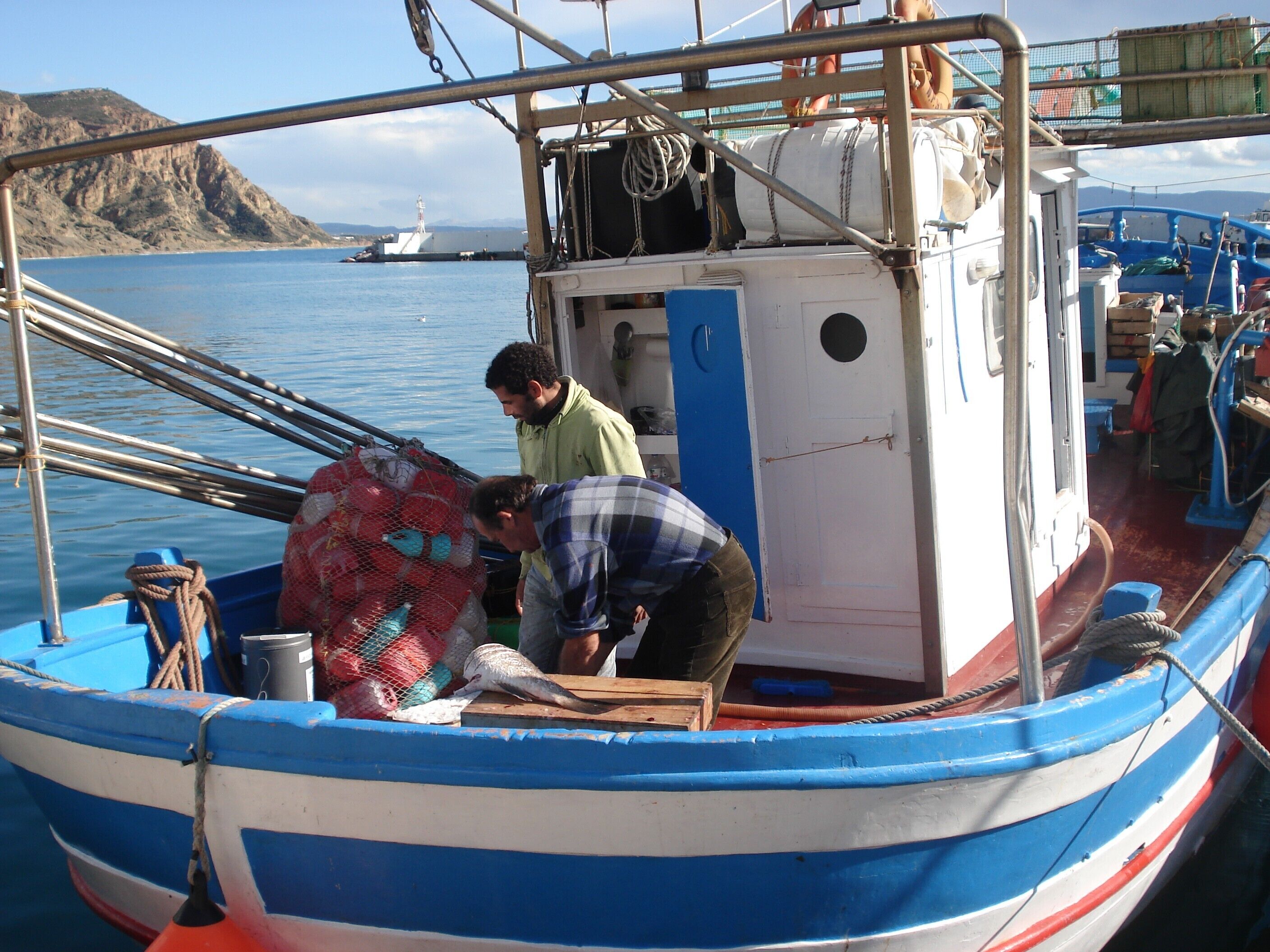 A boat with two people handling a fish, a net, and a wooden crate.