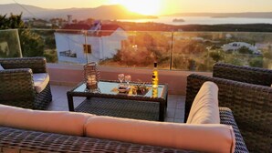 A balcony with wicker furniture, a glass table, and a bottle of wine.
