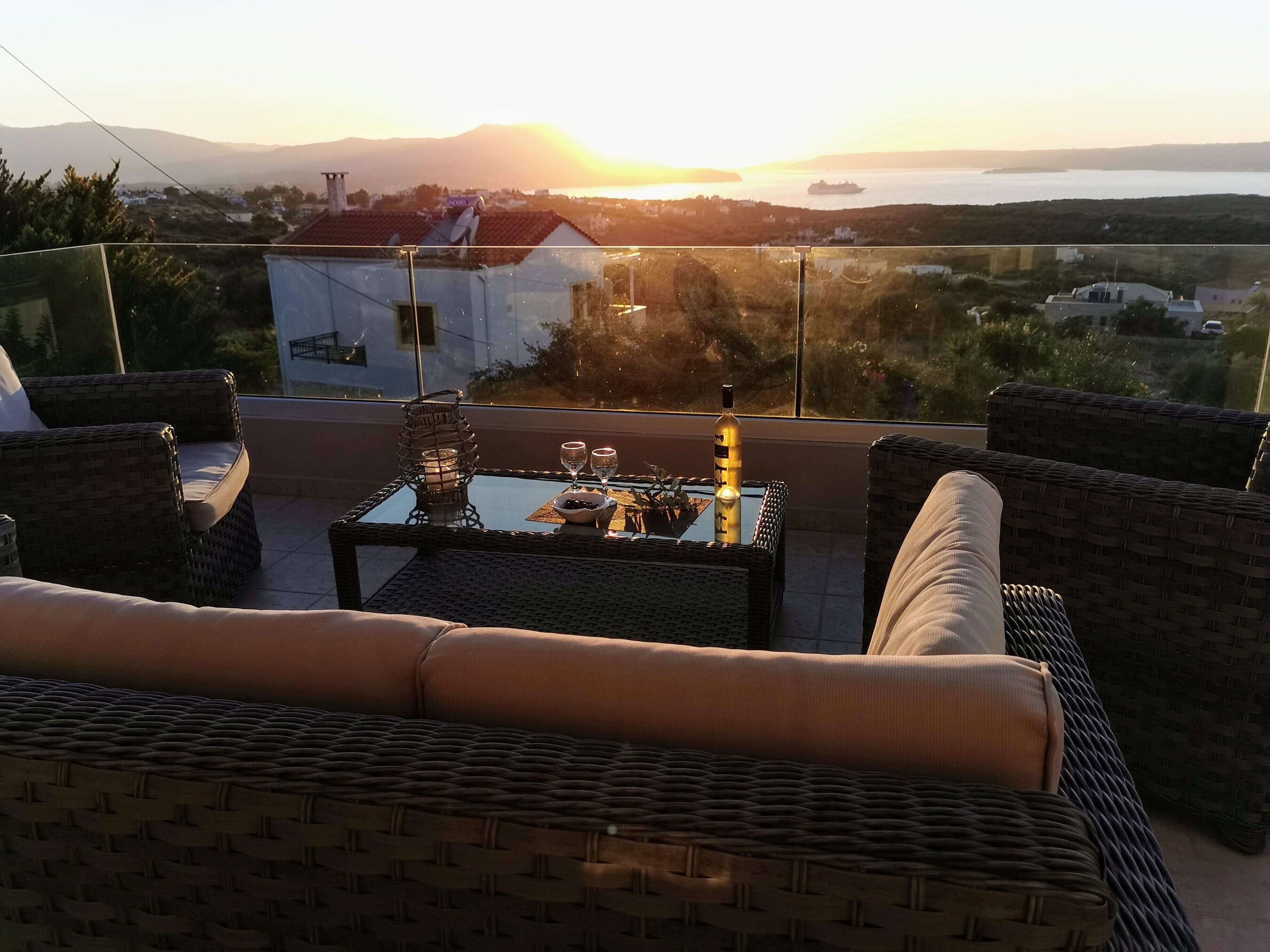 Un balcon agrémenté de meubles en osier, d’une table en verre et d’une bouteille.