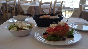 A table with a salad, a bread basket, and a glass of white wine.