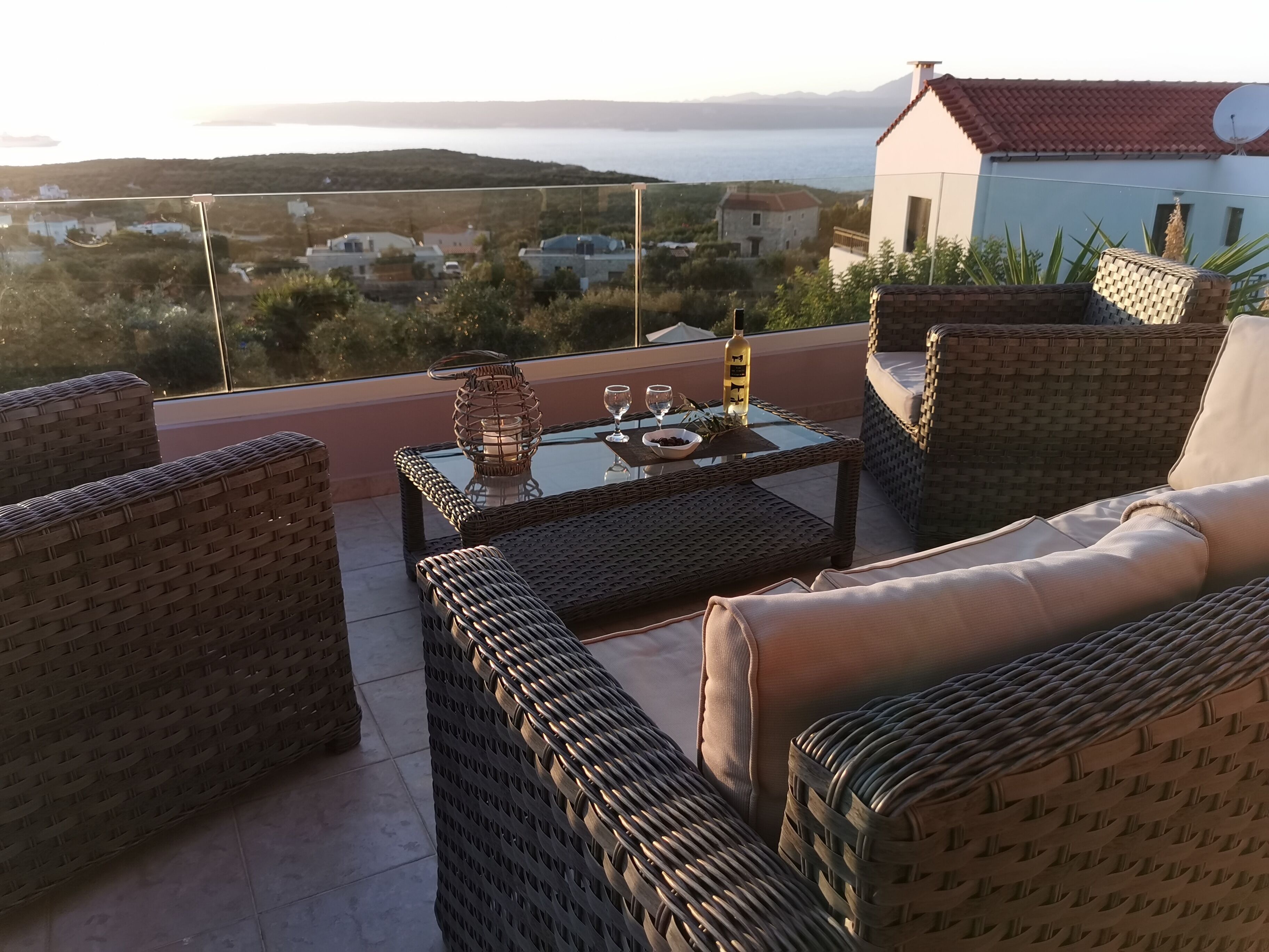 A balcony with wicker furniture, a glass table, and a bottle of wine.