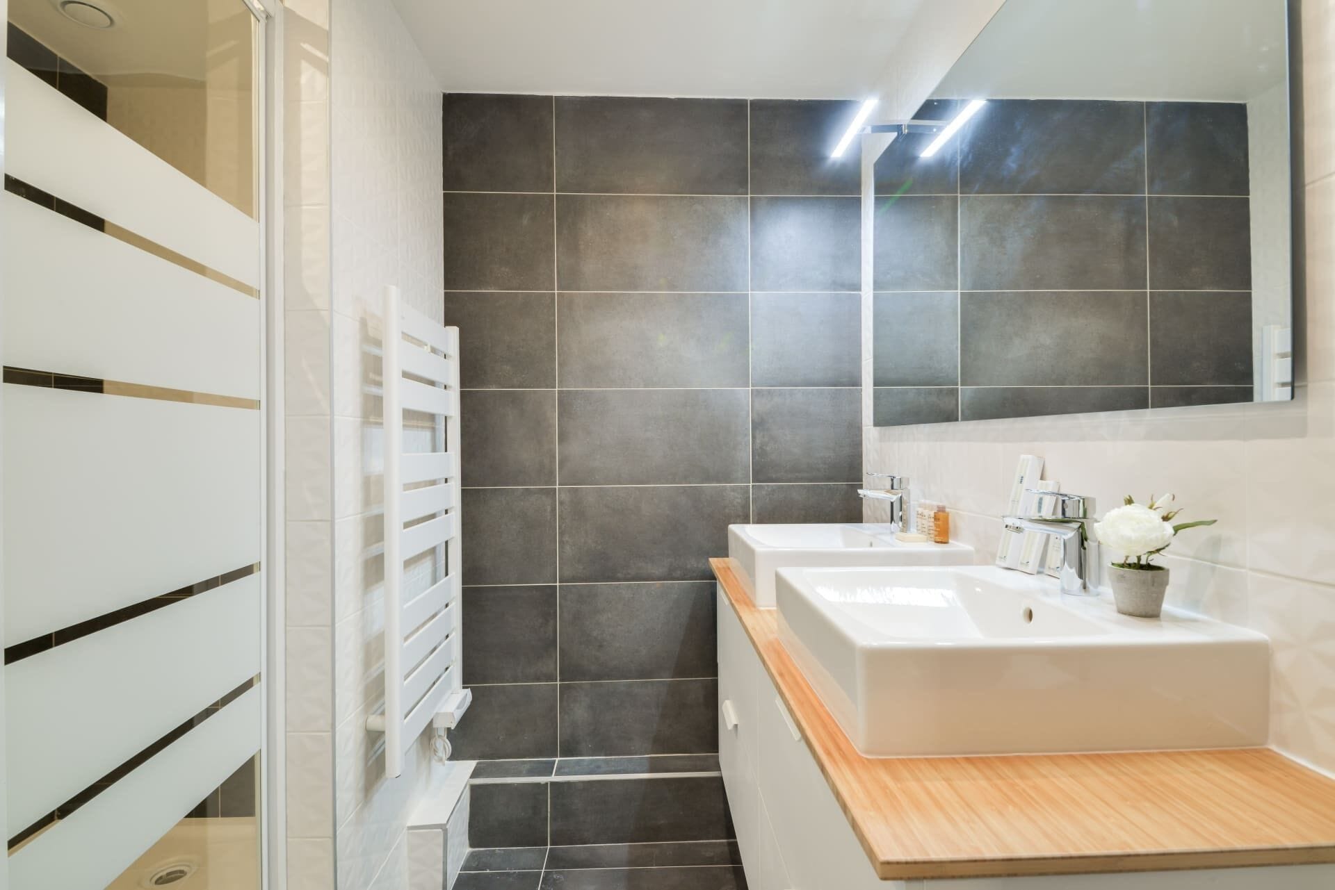 Une salle de bain moderne avec deux lavabos, un grand miroir et un espace douche.