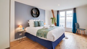 A modern bedroom with a large bed, a round mirror, a small table with a lamp, and a chair.