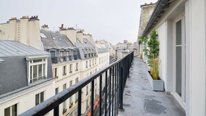 A narrow balcony with a metal railing, overlooking a row of terraced houses with varying roof styles and chimneys.