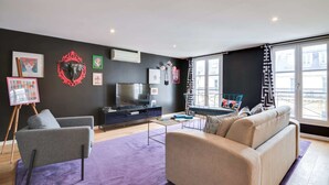 A modern living room with a large TV, a sofa, a chair, and artwork on the walls.
