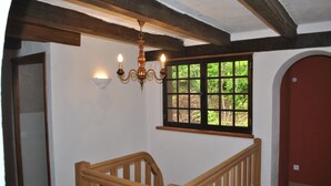 A staircase with wooden railings, a chandelier, and a window with a view of greenery.