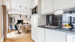 A modern kitchen with a black marble backsplash, a built-in dishwasher, and a dining area with a green sofa and wooden chairs.