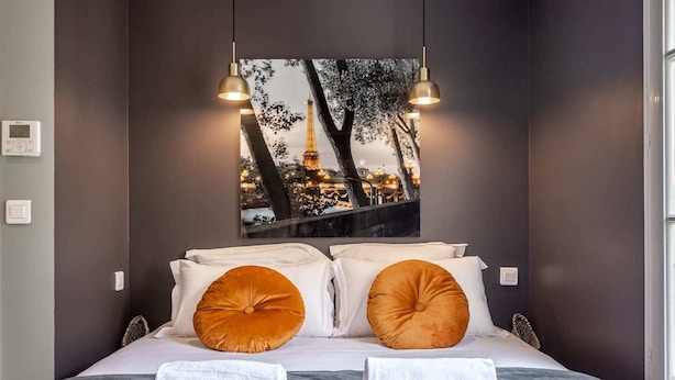 A hotel room with a bed, two pillows, a blanket, and a wall-mounted picture of the Eiffel Tower.