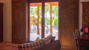 Una habitación con puerta de madera que da a un balcón con vistas a palmeras y una terraza de madera.