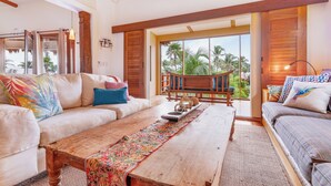 Un salón espacioso con una mesa de centro de madera, un sofá y una segunda zona de estar con vistas a palmeras.