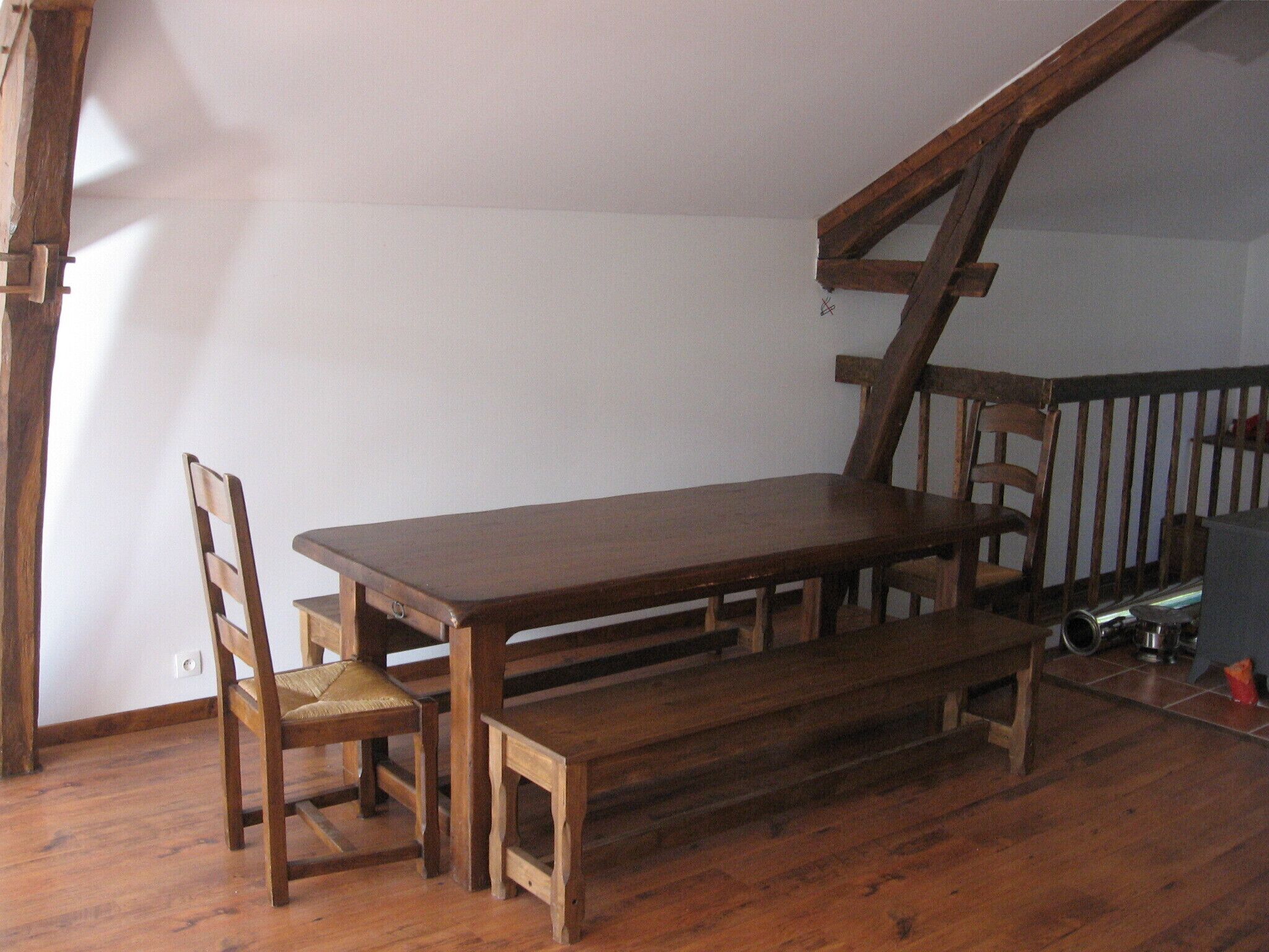 A wooden dining table with benches in a room with wooden flooring and a sloped ceiling.