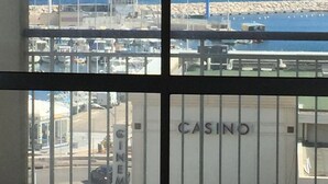 A view through a window with a metal railing, featuring a marina with boats, a building labeled "CASINO," and a clear blue sky. - 180 ° sea view apartment in Carry le Rouet (Carry-Le-Rouet)