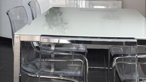 A dining area with a white table, clear chairs, a vase with white flowers, a painting of a bridge, and a lamp. - 180 ° sea view apartment in Carry le Rouet (Carry-Le-Rouet)