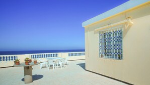 Een terras met een tafel, stoelen, plantenbakken en uitzicht op zee.