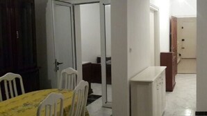 Een kamer met een eettafel en stoelen, een keuken met kastjes, en een houten deur.