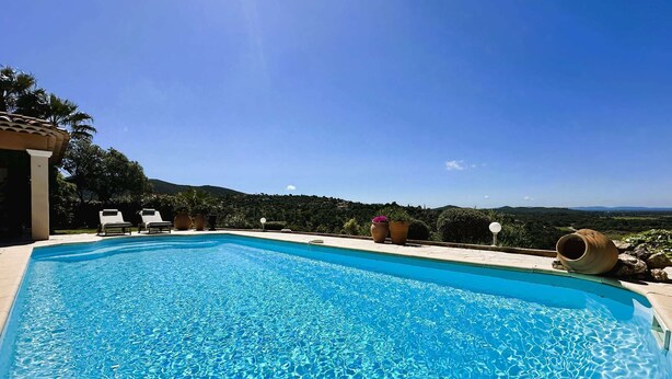 A swimming pool with clear blue water, surrounded by lounge chairs and potted plants, overlooking a scenic landscape.