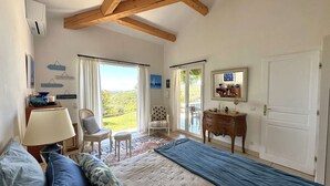 A bedroom with a bed, a chair, a dresser, and a view of the outdoors.