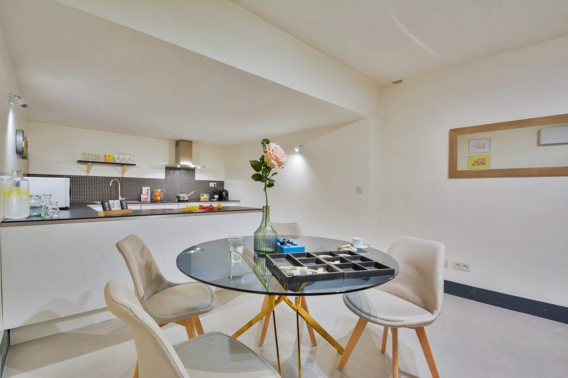 A modern kitchen with a black and white tiled backsplash, a white countertop, and a built-in oven. There is a round glass table with four chairs in the foreground.