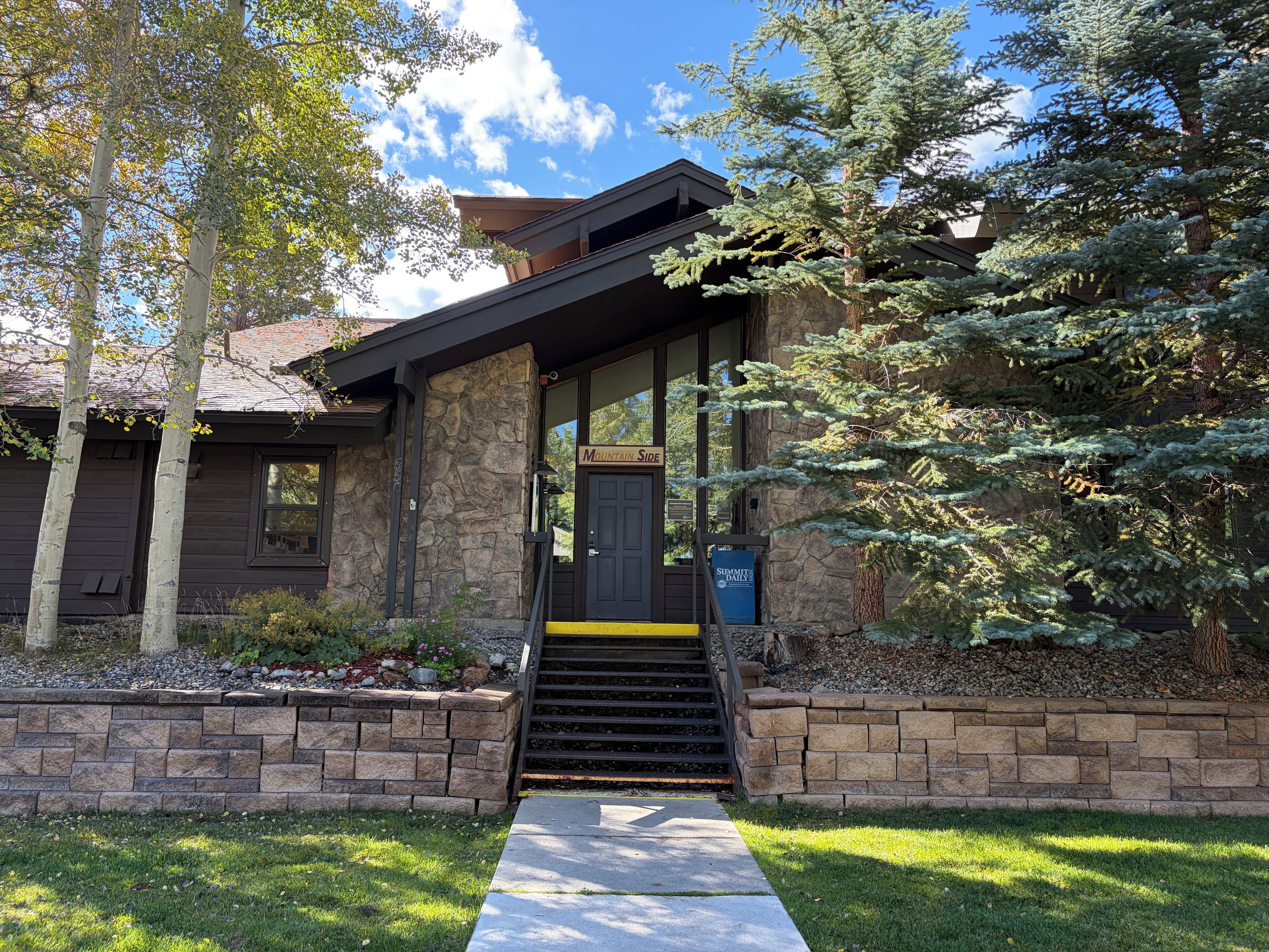 A two-story house with a stone facade, a front porch, and a sign that reads 'Summit Daily.'