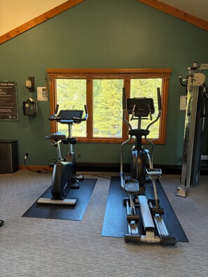 A gym with two cardio machines, a window with a view of trees, and a wall-mounted sign with rules. - Updated MountainSide Condo in The Heart of Frisco! (frisco)