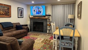 A living room with a fireplace, a television mounted above it, a sofa, a dining table with chairs, and a patterned rug. - Updated MountainSide Condo in The Heart of Frisco! (frisco)