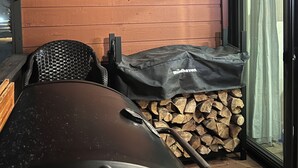 A covered outdoor seating area with a grill, a stack of firewood, and a wooden wall with a unique piece of driftwood. - Updated MountainSide Condo in The Heart of Frisco! (frisco)