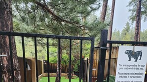 A fenced outdoor area with a dog standing behind the gate. - Christopher Creek Cabins - Cabin 5 (Payson)