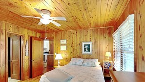 A wooden-paneled bedroom with a bed, bedside lamps, a ceiling fan, and a window with blinds. - Whitaker Sea La Vie | Soundfront Property, Great Views! (Topsail Beach)