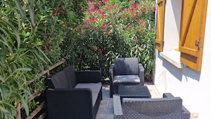 Un patio al aire libre con mobiliario de mimbre, una valla de madera y un edificio blanco con contraventanas de madera.