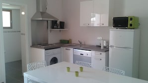 Una cocina compacta con lavadora, lavavajillas, microondas y un pequeño comedor con mesa y sillas.