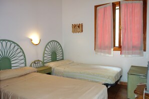 Une chambre avec deux lits simples, une table de chevet, un fauteuil vert, une petite armoire et un luminaire fixé au mur.