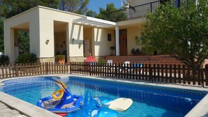 A swimming pool with inflatable toys, a wooden fence, and a building with a balcony. - Villa with private protected pool, 200 m from the beach, air conditioning  (Ametlla de Mar)