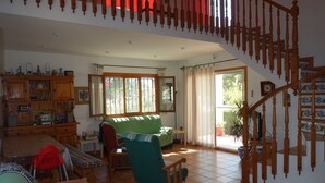 A spacious living room with a wooden staircase, a green sofa, a wooden rocking chair, and a dining area with a table and chairs. - Villa with private protected pool, 200 m from the beach, air conditioning  (Ametlla de Mar)