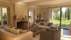 A living room with a fireplace, sofas, a coffee table, and a view of the garden. - Provencal farmhouse from the 19th century with swimming pool, charming house (Aix-En-Provence)