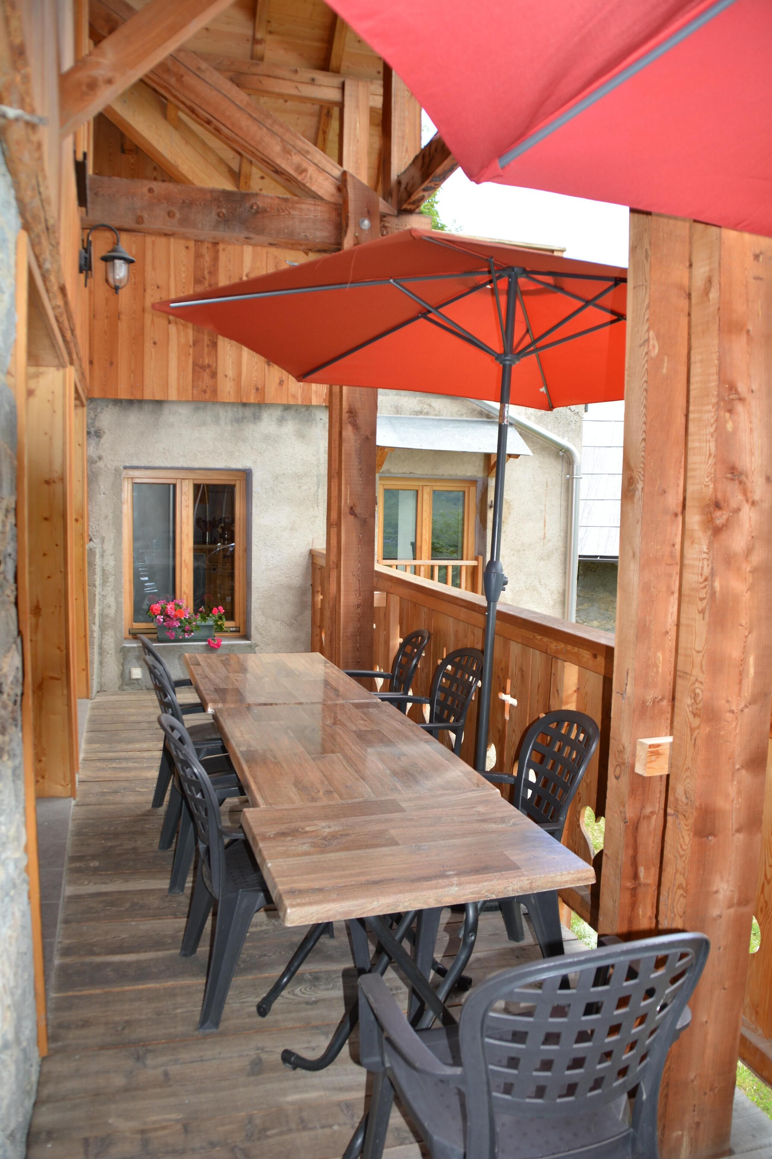 A wooden deck with a long table and chairs, an umbrella, and a lantern.